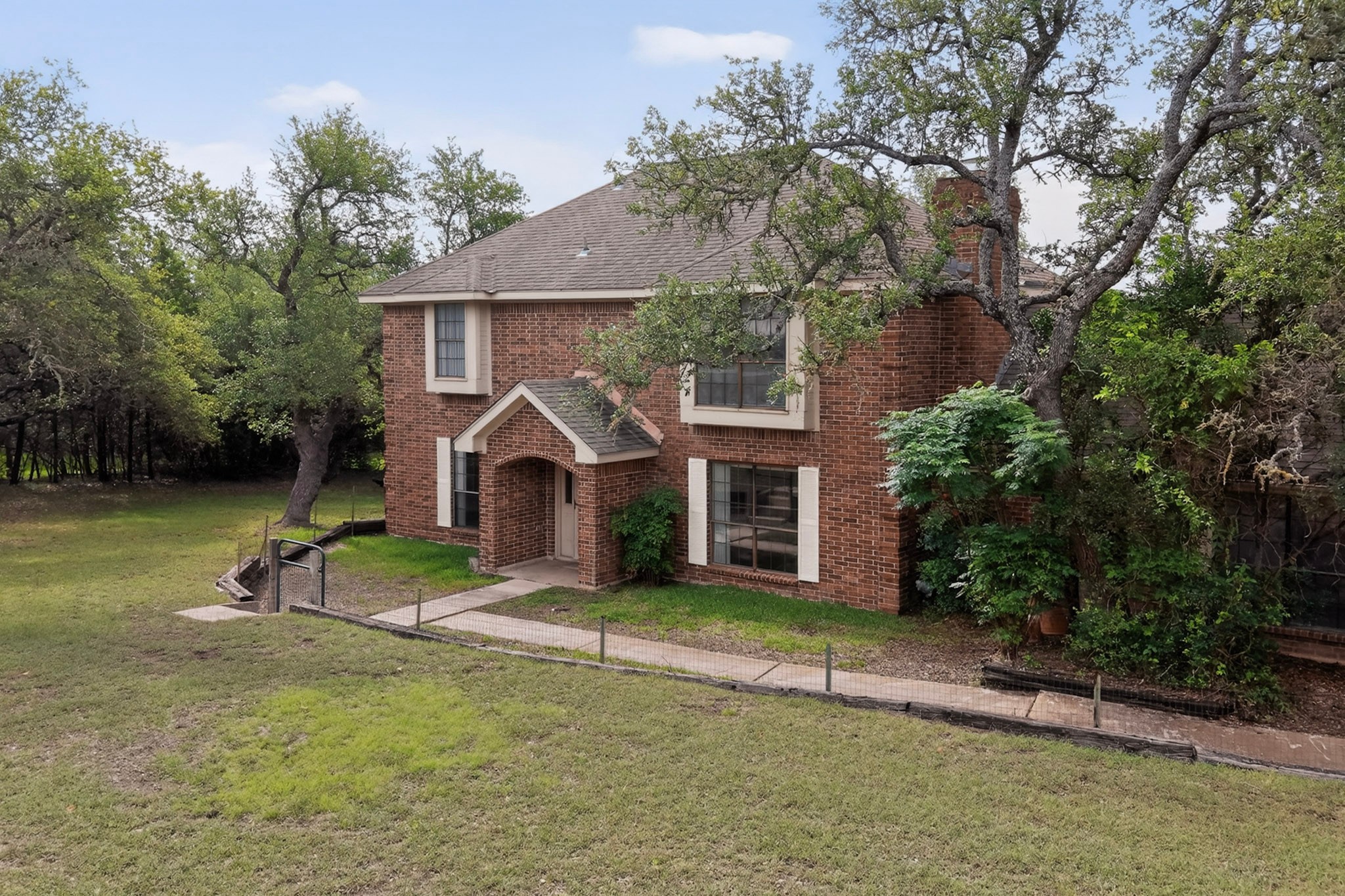 1003 Pier Branch Road Dripping Springs, TX 78620 - Photo 11 of 40 Mature trees frame this traditional brick residence, offering a welcoming entry with an arched portico.