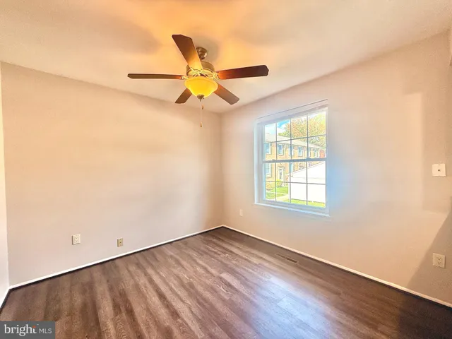an empty room with wooden floor fan and windows