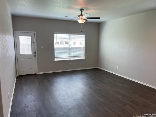 an empty room with wooden floor chandelier fan and windows