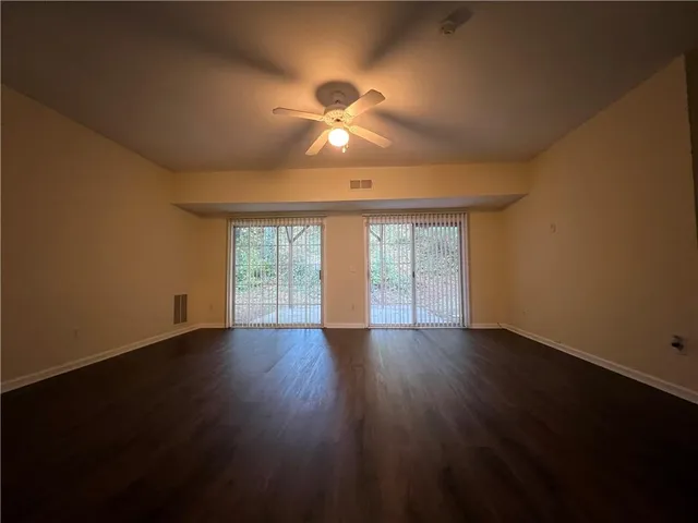 a view of an empty room with wooden floor and a ceiling fan