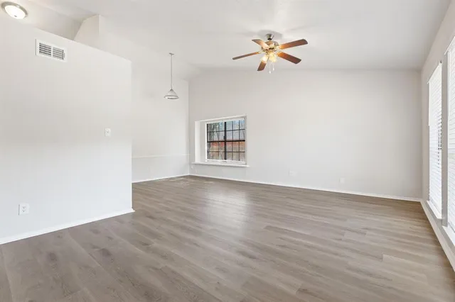 an empty room with wooden floor chandelier fan and windows