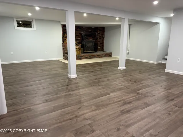 an empty room with wooden floor and way to kitchen