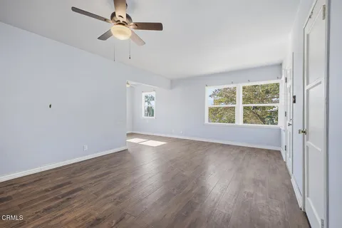 an empty room with wooden floor chandelier fan and windows