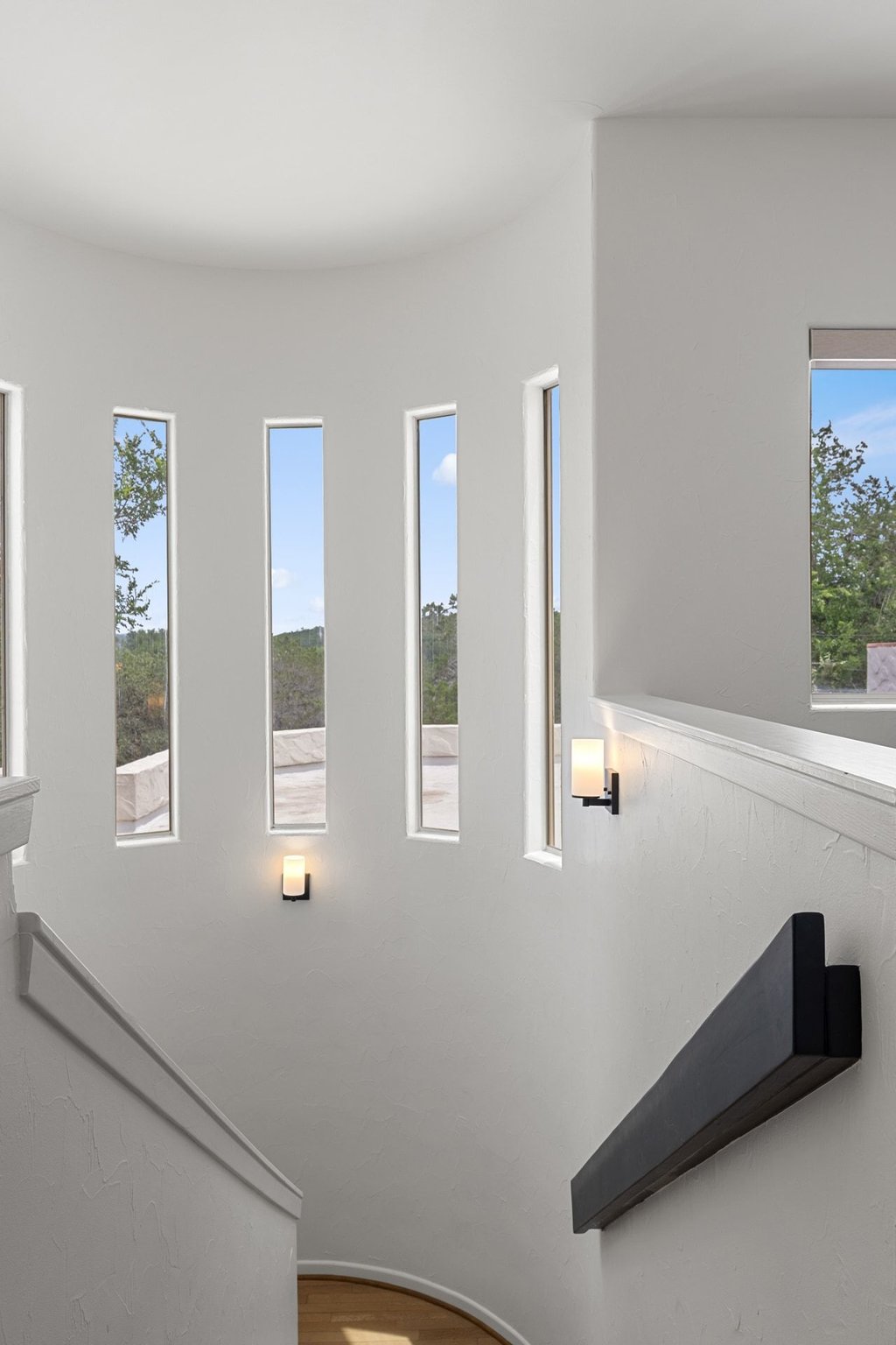 716 North Commons Ford Road Austin, TX 78733 - Photo 18 of 30 Curved staircase with a contemporary black handrail and white wall-mounted sconces