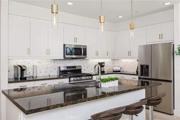 a kitchen with granite countertop a refrigerator a sink and white cabinets