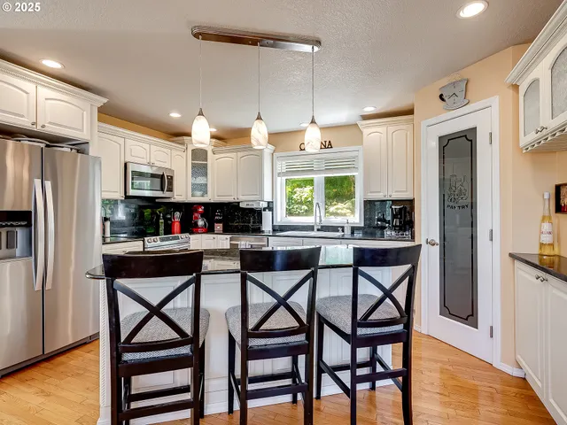 a kitchen with stainless steel appliances granite countertop a stove a refrigerator a microwave a dining table and chairs with wooden floor