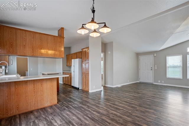 20150 Enoch Road Colorado Springs, CO 80928 - Photo 14 of 50 Kitchen featuring lofted ceiling, freestanding refrigerator, dark wood-style flooring, light countertops, and brown cabinets