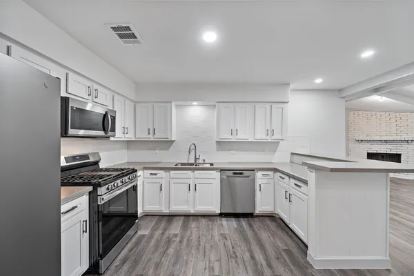 a kitchen with stainless steel appliances a sink dishwasher a stove top oven a refrigerator with white cabinets and wooden floor