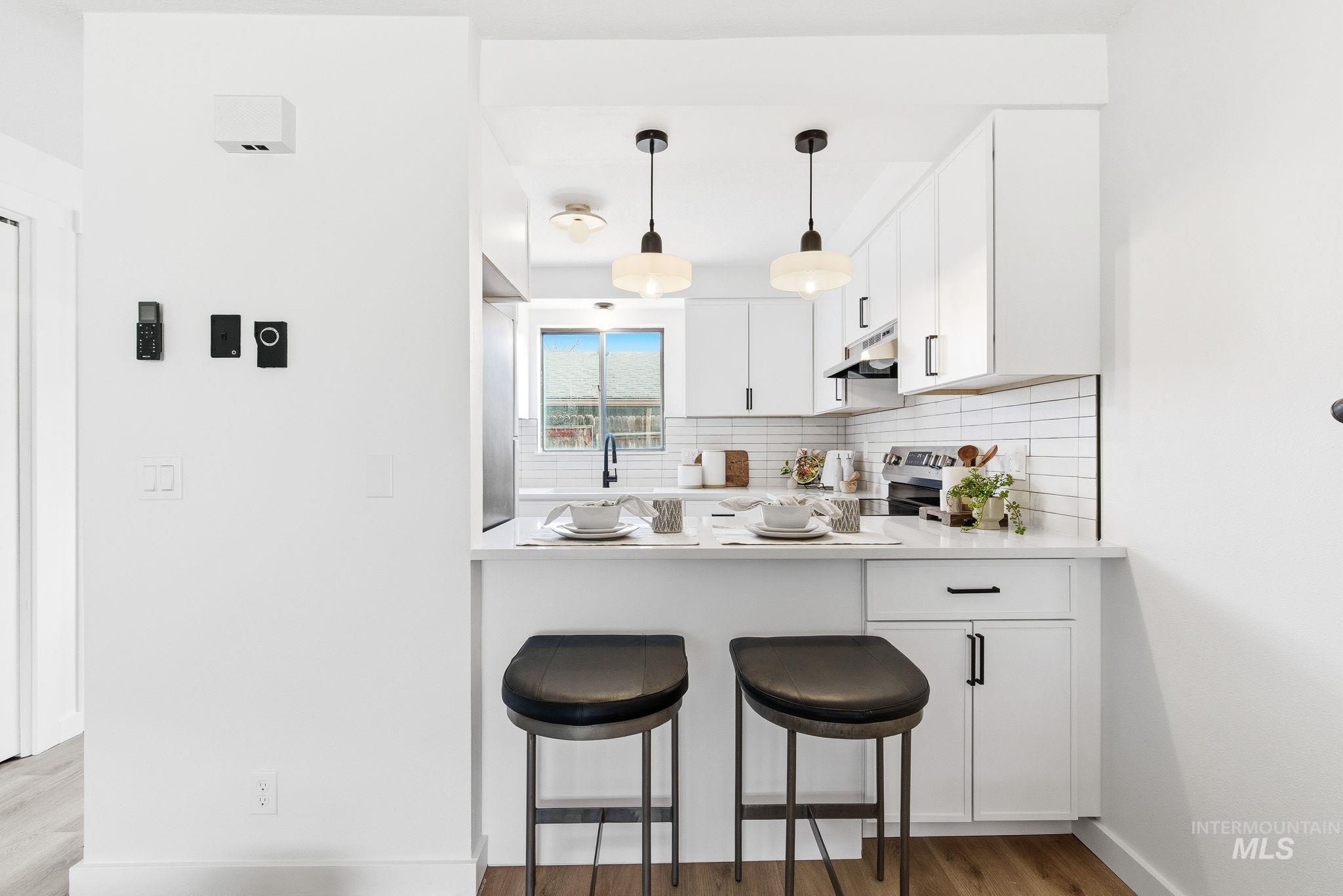 8443 West Rifleman Street Boise, ID 83704 - Photo 11 of 39 Kitchen with white cabinets, backsplash, light wood-style floors, pendant lighting, and a kitchen bar