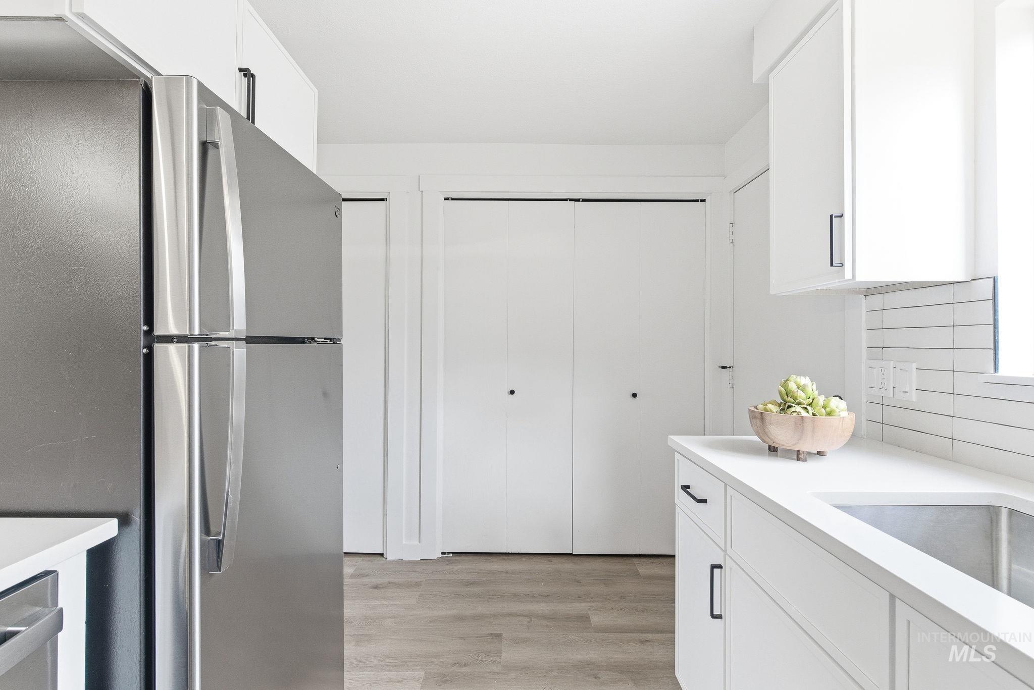 8443 West Rifleman Street Boise, ID 83704 - Photo 18 of 39 Kitchen featuring white cabinetry, freestanding refrigerator, light wood-style floors, and decorative backsplash