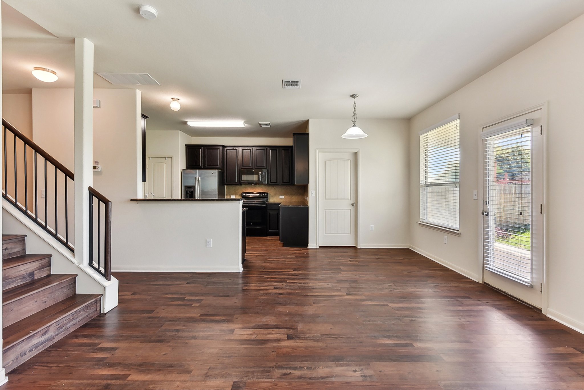 310 Potters Peak Way Georgetown, TX 78626 - Photo 7 of 21 Open-concept living area featuring wood-finish flooring, a contemporary staircase with dark wood treads and balusters, and a kitchen with dark cabinetry and stainless steel appliances