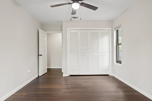 an empty room with wooden floor ceiling fan and window