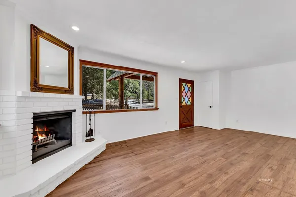 a view of an empty room with wooden floor fireplace and a window