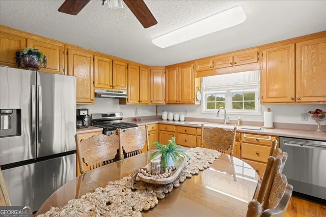 a kitchen with stainless steel appliances granite countertop a refrigerator a sink dishwasher a dining table and chairs with wooden floor