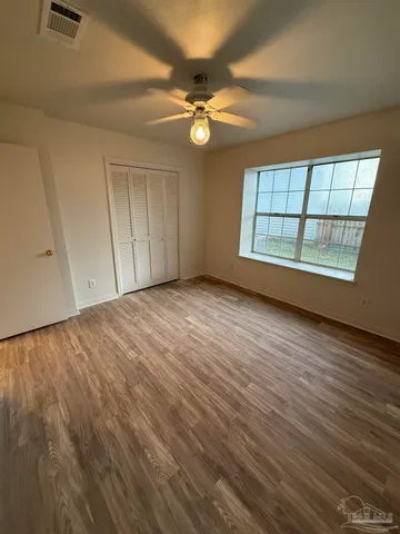 an empty room with wooden floor fan and windows