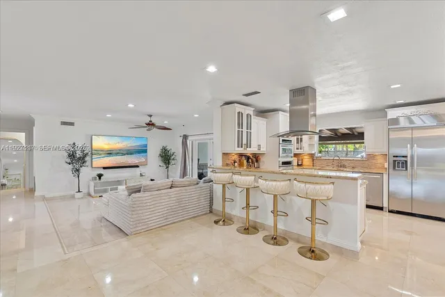 a kitchen with stainless steel appliances kitchen island granite countertop a refrigerator a stove a sink and white cabinets with wooden floor