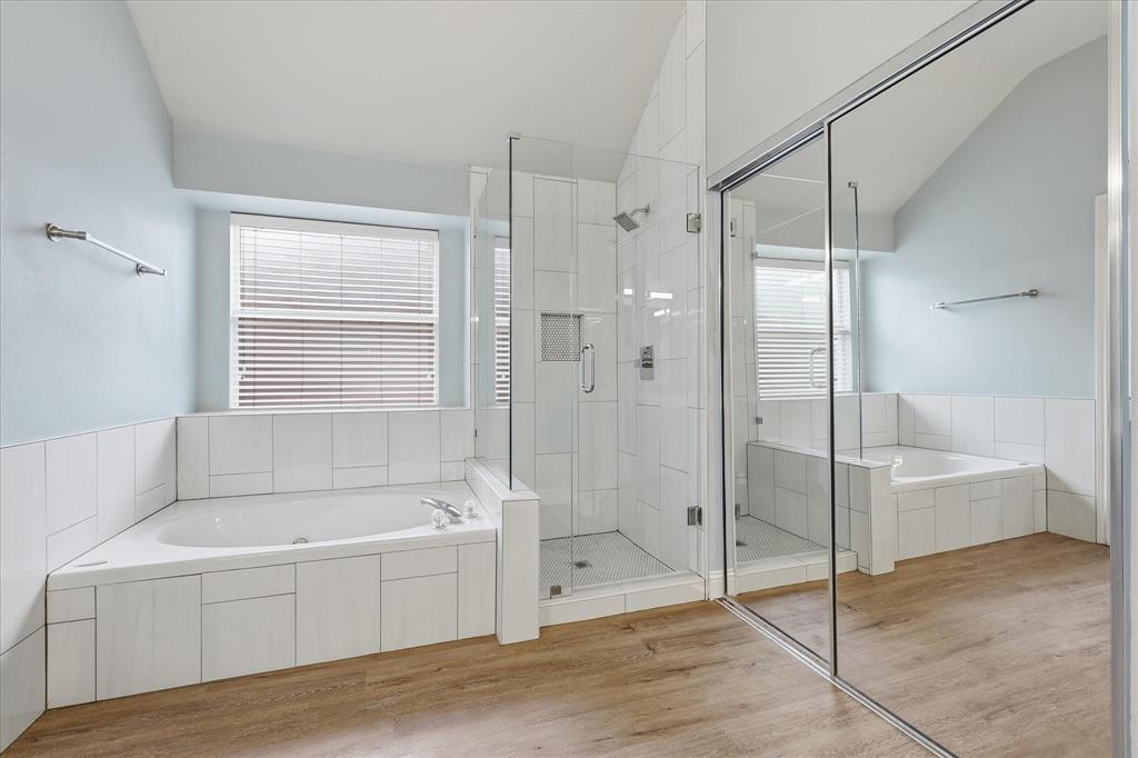 2616 Hollow Ridge Drive Denton, TX 76210 - Photo 21 of 31 Corner soaking tub with white tile surround, glass-enclosed walk-in shower with white tile, wood-finish flooring, and a mirrored sliding door