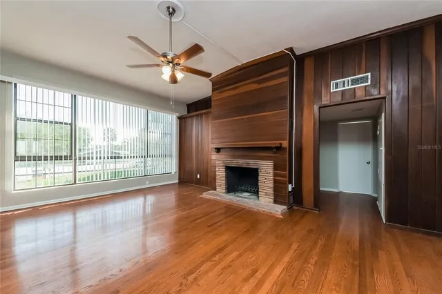 a view of an empty room with wooden floor fireplace and a window