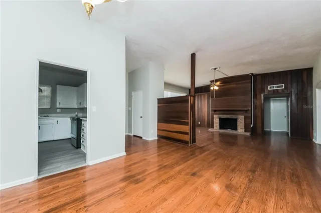 a view of empty room with wooden floor and kitchen view