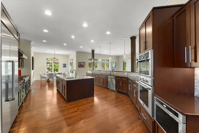 a kitchen with stainless steel appliances granite countertop a refrigerator a sink dishwasher a stove and a dining table with wooden floor