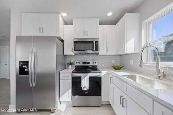 a kitchen with stainless steel appliances granite countertop a refrigerator a stove a sink and white cabinets