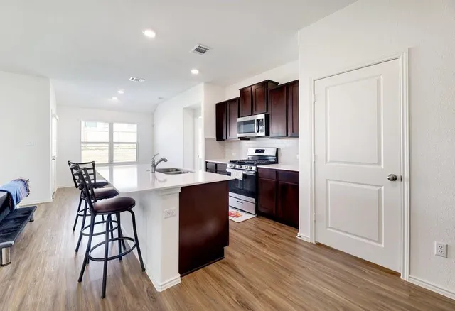 a kitchen with stainless steel appliances granite countertop a stove top oven a sink dishwasher and a microwave with wooden floor