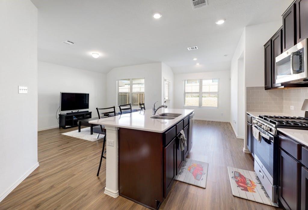 21416 Bird Wing Drive Pflugerville, TX 78660 - Photo 10 of 25 a kitchen with stainless steel appliances granite countertop a stove top oven a sink dishwasher and a microwave with wooden floor
