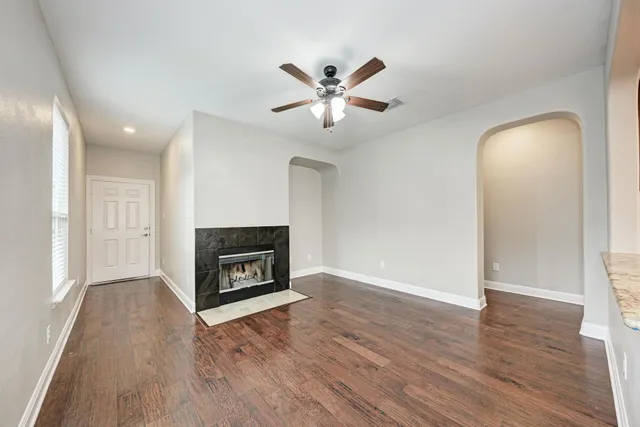 an empty room with wooden floor a ceiling fan a fireplace and windows