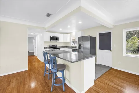 a kitchen with stainless steel appliances granite countertop a refrigerator a stove top oven a sink dishwasher and white cabinets with wooden floor