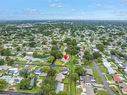 a sign that is sitting in front of a house with plants and trees