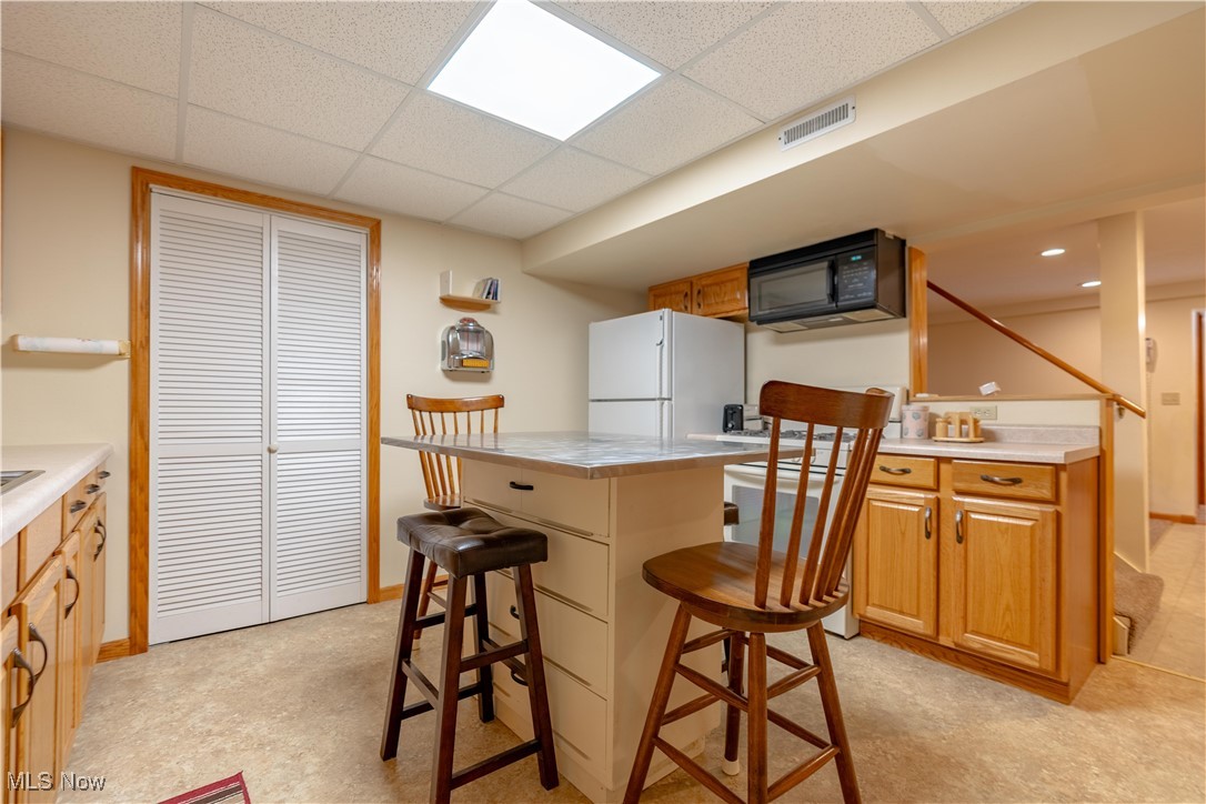 1766 Far View Road Akron, OH 44312 - Photo 23 of 33 Lower level Kitchen featuring a kitchen bar, a drop ceiling, black microwave, freestanding refrigerator, and light countertops