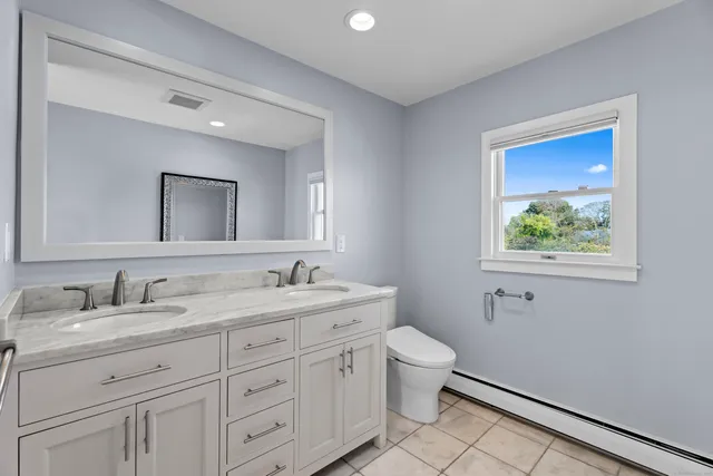 a bathroom with a granite countertop toilet a sink a mirror and a window