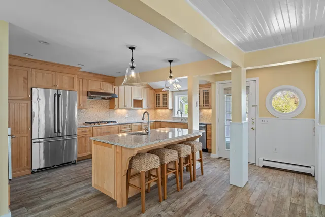 a kitchen with stainless steel appliances granite countertop a refrigerator a stove a sink dishwasher and a dining table with wooden floor