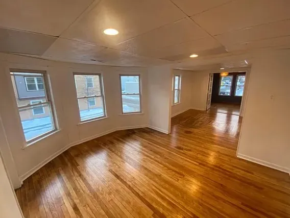 a view of an empty room with wooden floor and a window