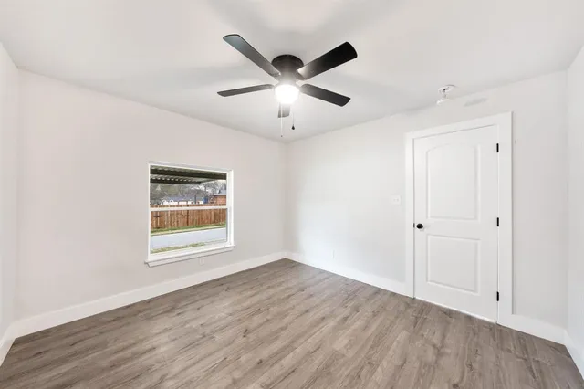 a view of an empty room with wooden floor and a ceiling fan