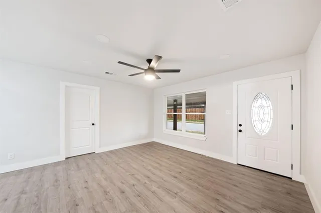 an empty room with wooden floor chandelier fan and windows