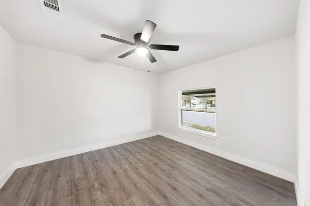 an empty room with wooden floor ceiling fan and windows