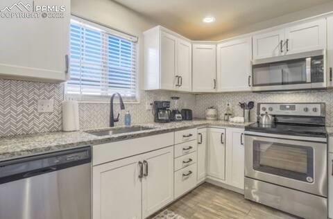 6564 Watusi Road Peyton, CO 80831 - Photo 3 of 12 a kitchen with granite countertop white cabinets white stainless steel appliances and a sink