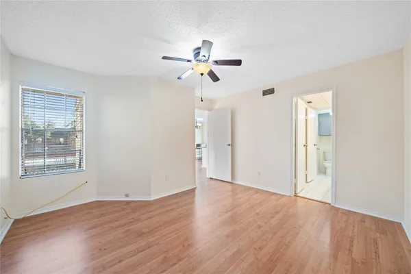 an empty room with wooden floor ceiling fan and windows
