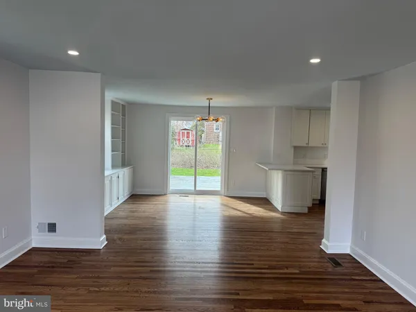 a view of empty room with wooden floor and kitchen