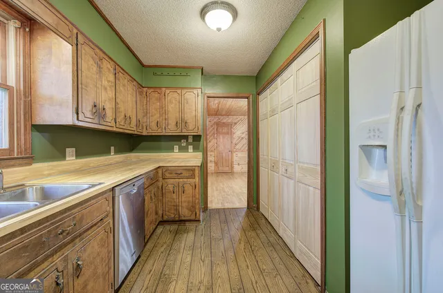 a kitchen with stainless steel appliances granite countertop a refrigerator a sink dishwasher a stove and white countertops with wooden floor