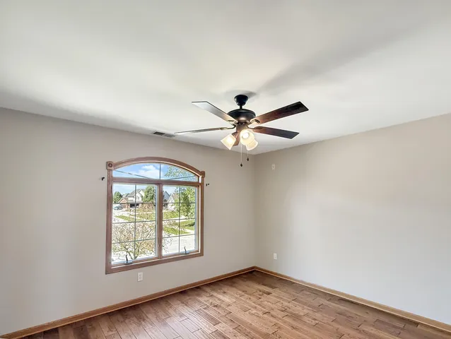an empty room with wooden floor fan and windows