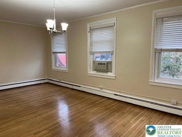 an empty room with wooden floor chandelier and windows