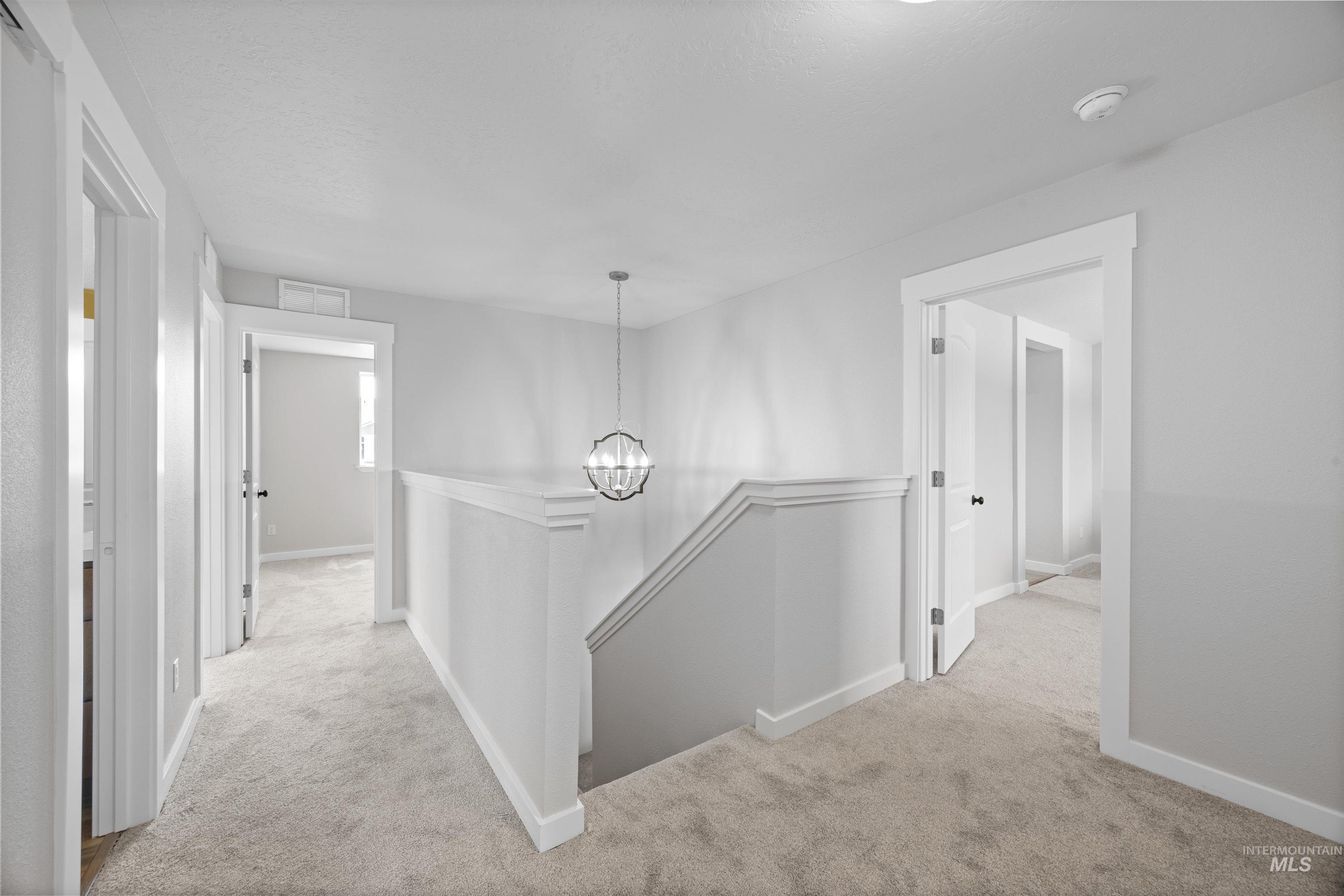 300 South Rocker Avenue Kuna, ID 83634 - Photo 19 of 49 Spacious carpeted hallway featuring a contemporary globe pendant light, white painted walls, white baseboards, and multiple doorways