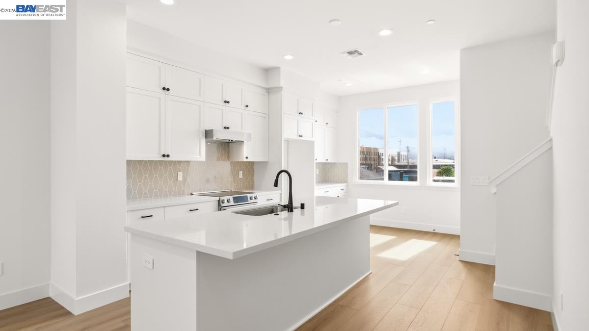 a kitchen with stainless steel appliances a sink a stove and white cabinets with wooden floor