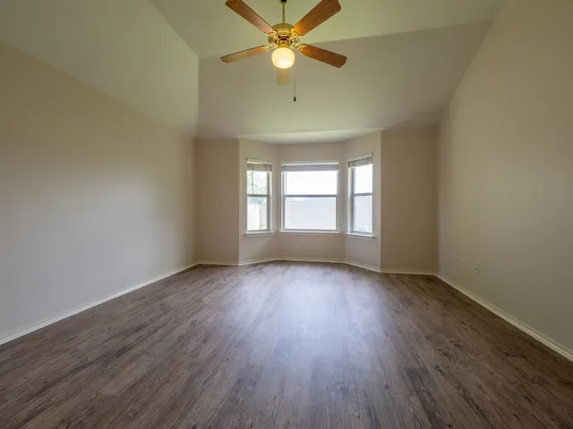 an empty room with wooden floor fan and windows