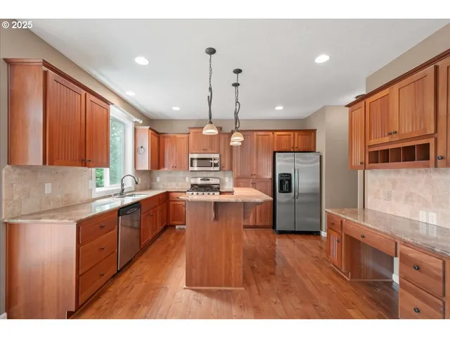 a large kitchen with stainless steel appliances wooden floor and a window