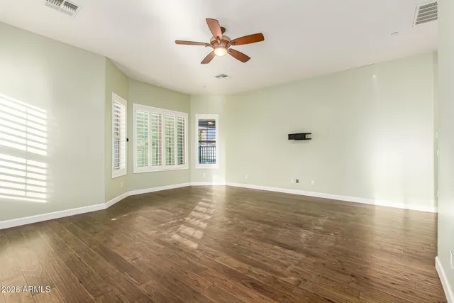 a view of an empty room with wooden floor and a ceiling fan