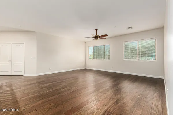 an empty room with wooden floor chandelier fan and windows