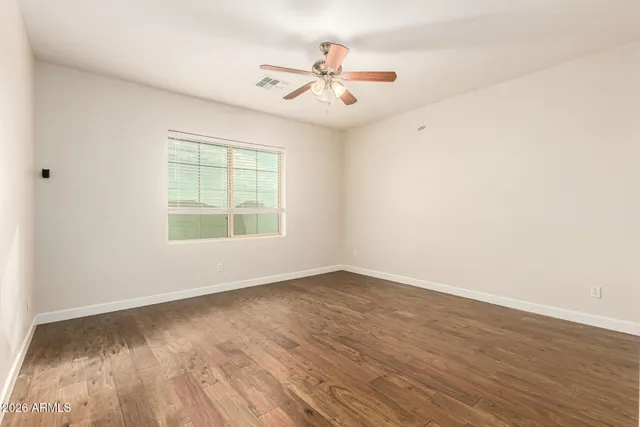 an empty room with wooden floor ceiling fan and windows